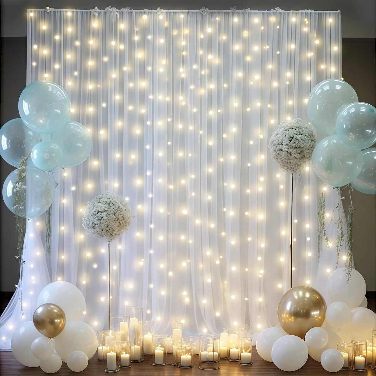 A backdrop featuring sheer white tulle curtains illuminated by warm string lights and surrounded by various clear and white b