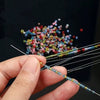A hand holds a set of ultra-fine beading needles with various colored threads for jewelry making.