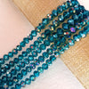 A strand of faceted blue-green crystal glass spacer beads is laid out on a beige fabric background.