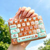 A hand holds a colorful cartoon keycap fidget keychain with various pastel-colored buttons outdoors.