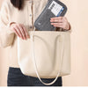 A woman holds a beige leather tote bag and an RFID-blocking passport holder.
