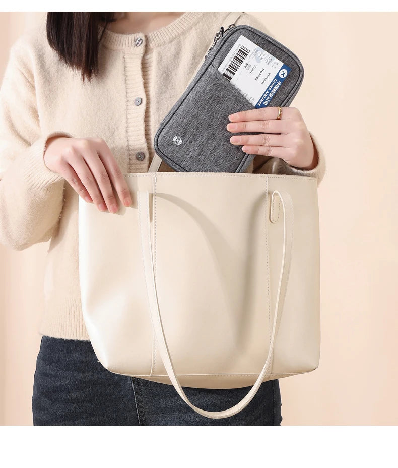 A woman holds a beige leather tote bag and an RFID-blocking passport holder.