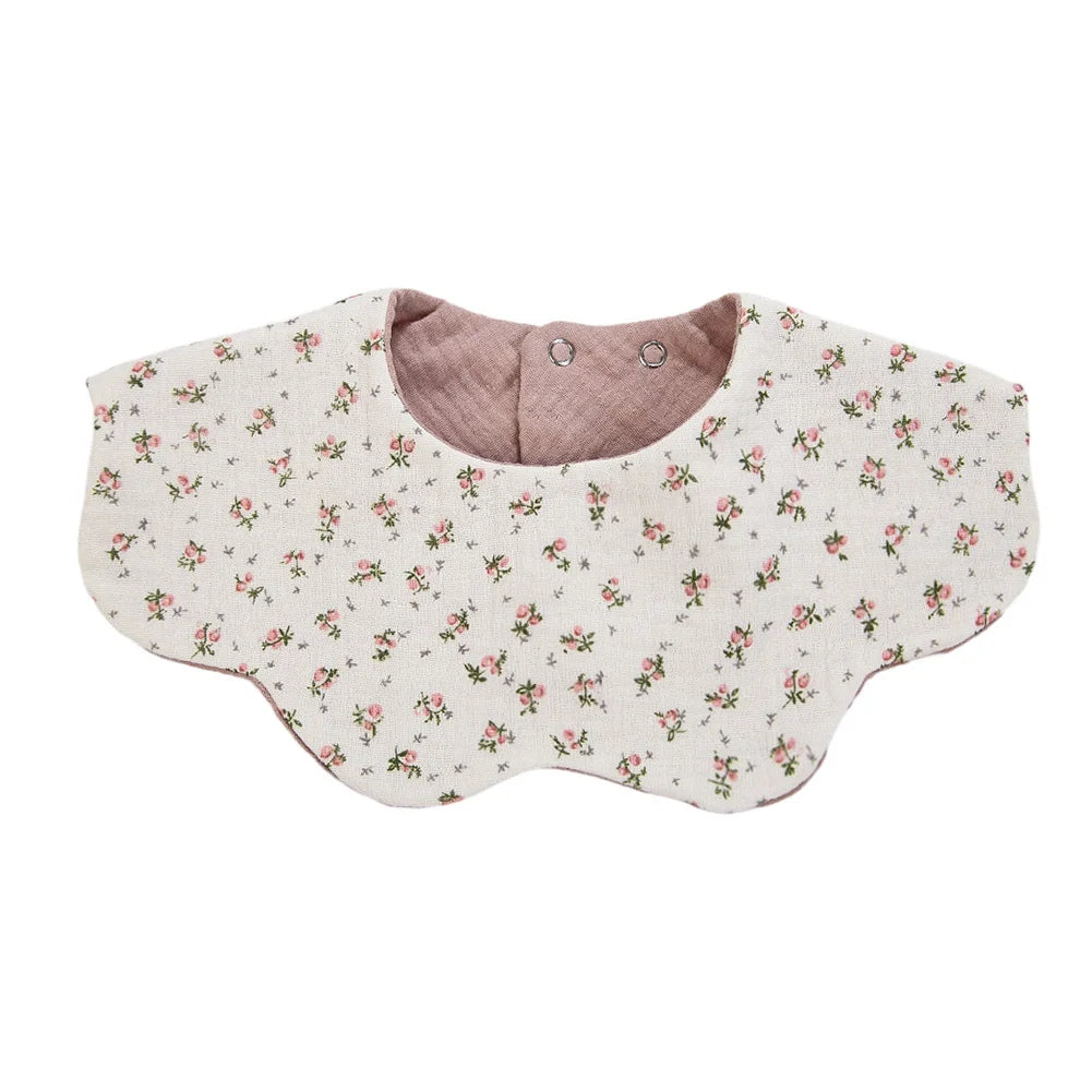 A light floral patterned muslin cotton baby bib with a pink lining and adjustable snap closure.