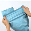 A hand is holding a light blue heavy-duty waterproof poly mailer bag, showing its flexible and protective nature.