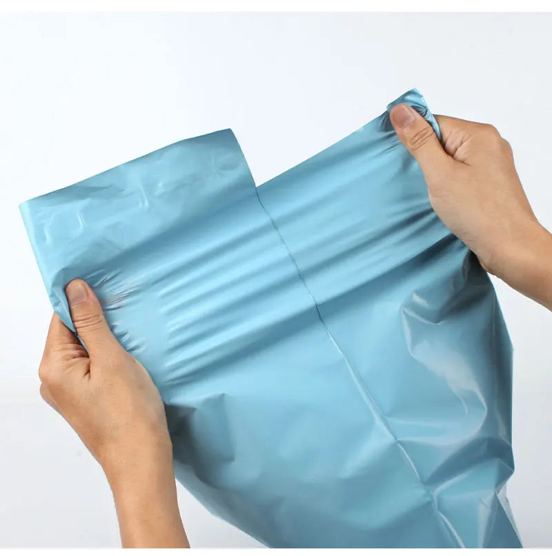 A hand is holding a light blue heavy-duty waterproof poly mailer bag, showing its flexible and protective nature.