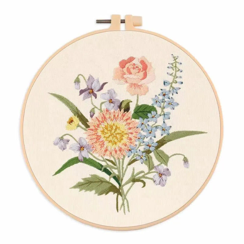 A circular embroidery hoop featuring a floral design of pink and blue wildflowers on natural linen fabric.