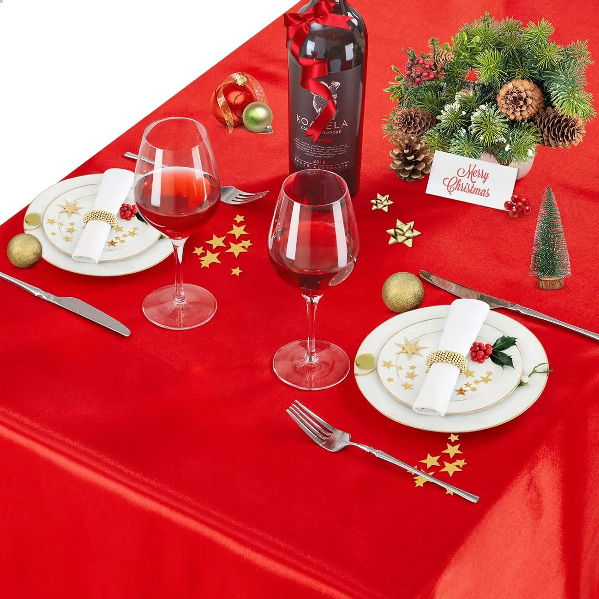 A red satin tablecloth set for dining featuring a wine glass, a bottle, and silverware with Christmas decorations.