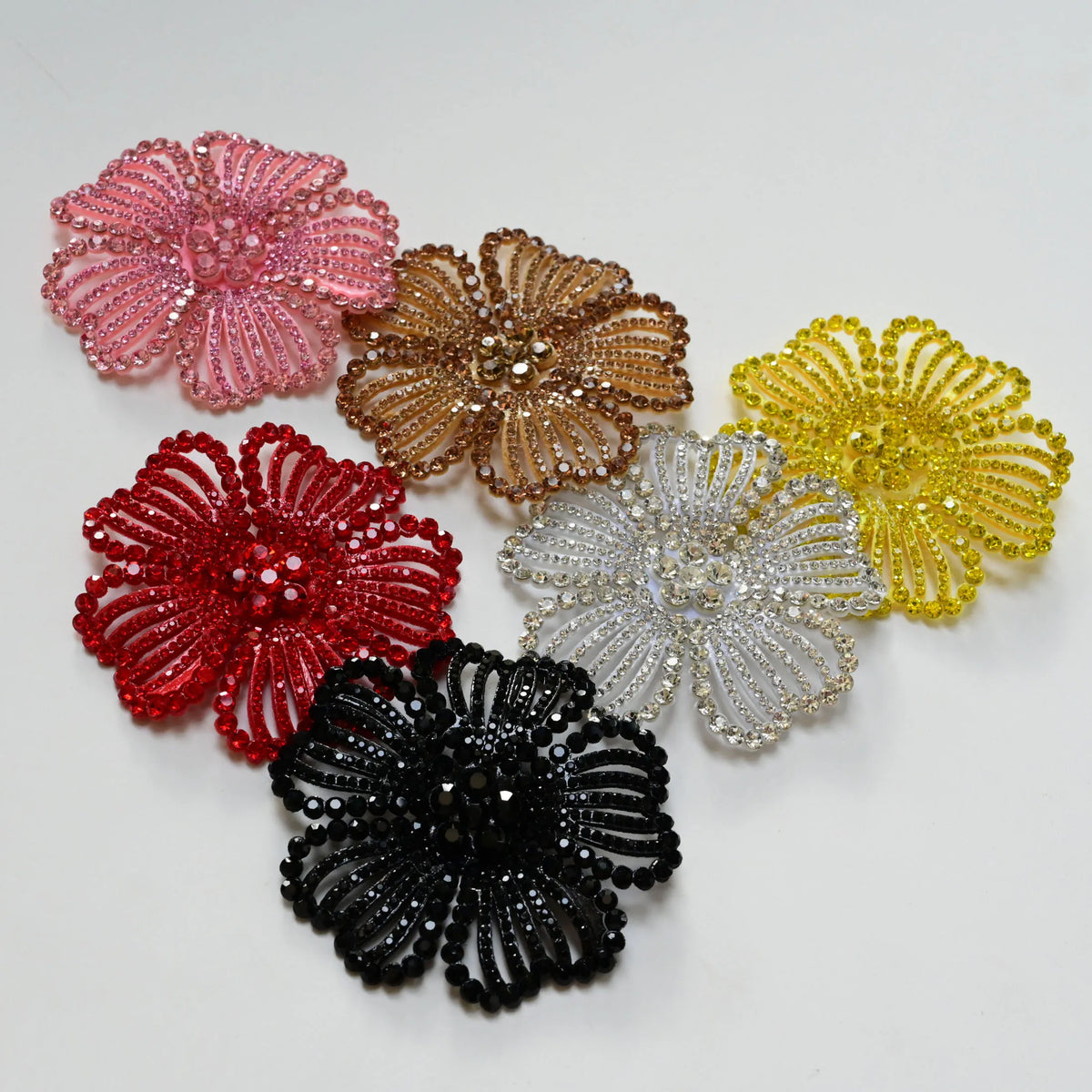 A collection of nine crystal rhinestone flower sew-on patches in shades of pink, gold, yellow, red, and black.