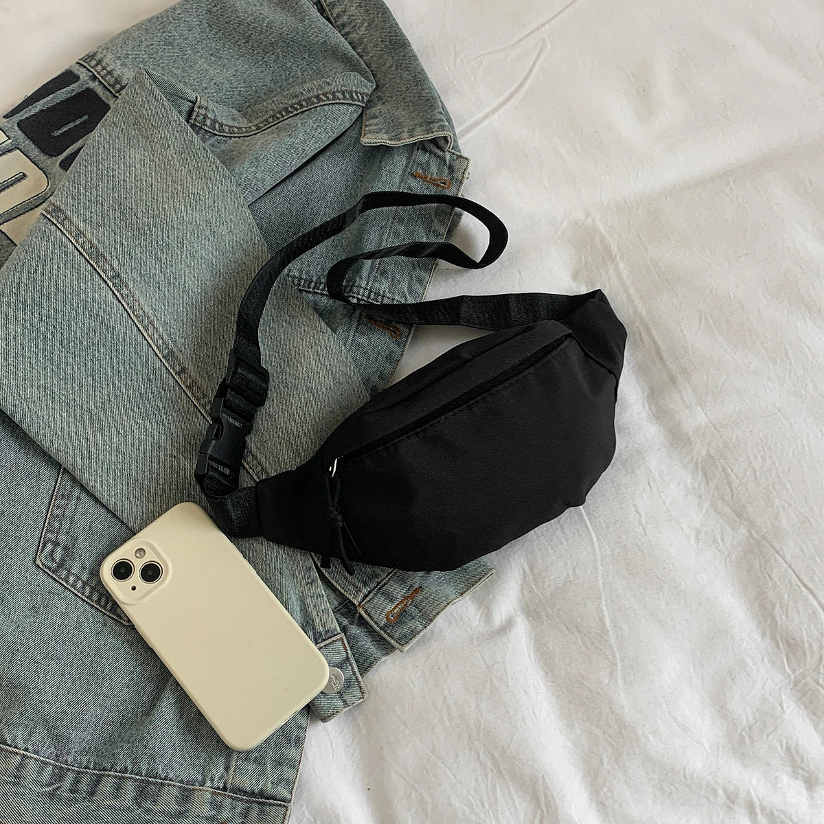 Un bolso cruz de nylon negro colocado sobre una chaqueta de mezclilla gris claro y una camisa blanca.