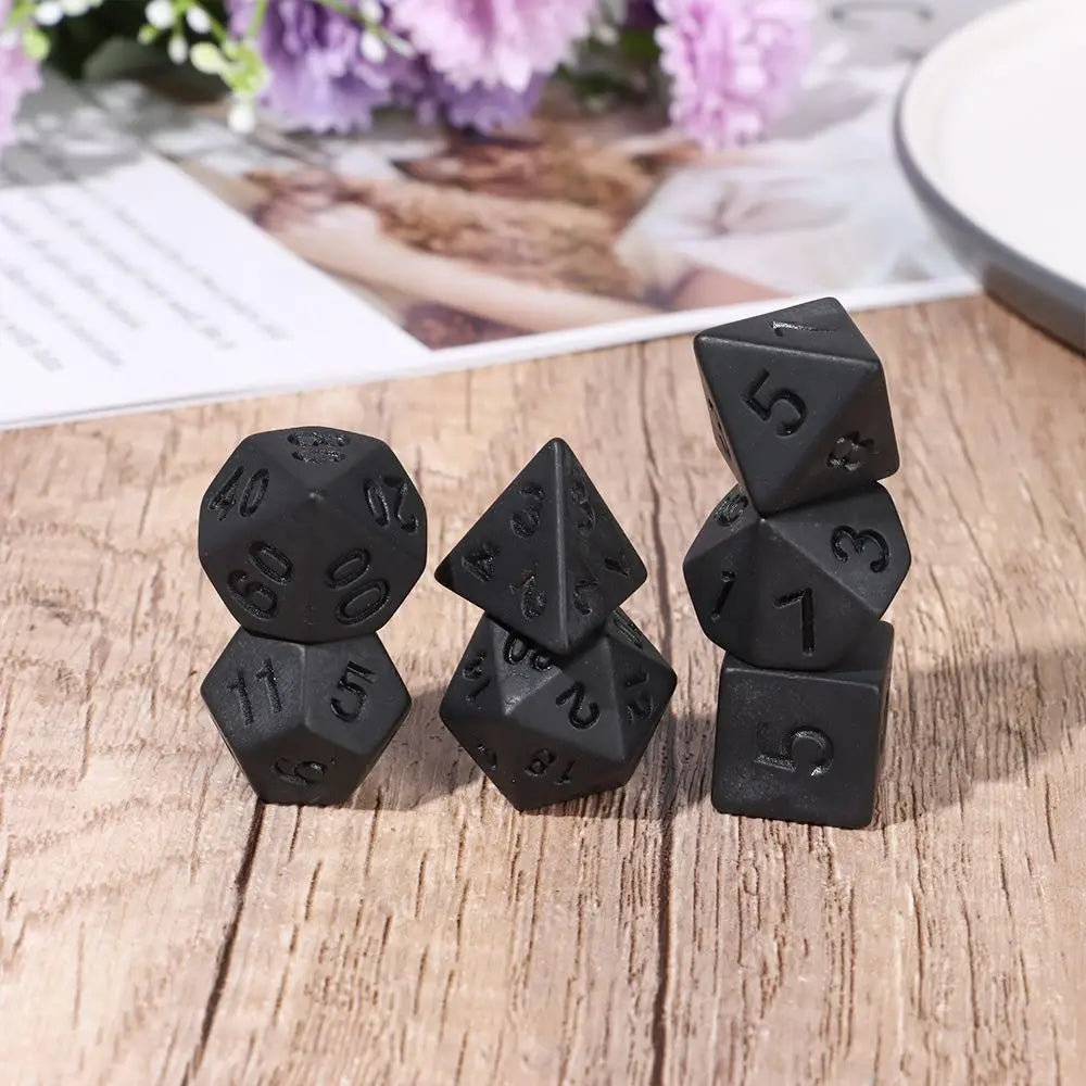 A set of matte black polyhedral dice including d10, d6, d8, d12, and d20 resting on a wooden surface.