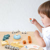 A young child is playing with a wooden spelling word game featuring letter tiles and a bear figure on a wooden table.