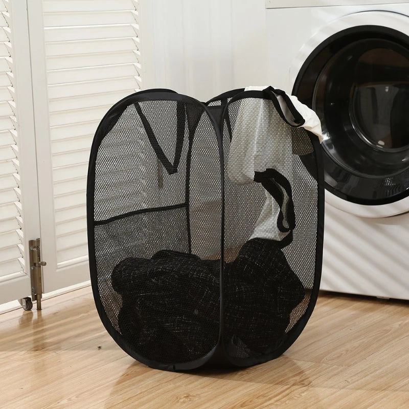 A black foldable laundry hamper with a mesh design is shown next to a white washing machine.
