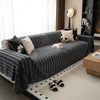 A dark gray woven sofa cover with black stripes is draped over a sofa in a bright living room.