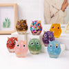 A collection of handcrafted crystal owl figurines in various colors and finishes displayed on a white surface.