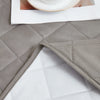 A close-up of a gray waterproof mattress protector with quilted texture and elastic straps, placed on a white surface.