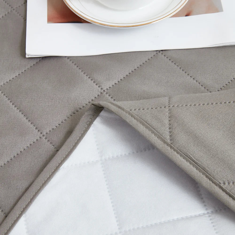 A close-up of a gray waterproof mattress protector with quilted texture and elastic straps, placed on a white surface.