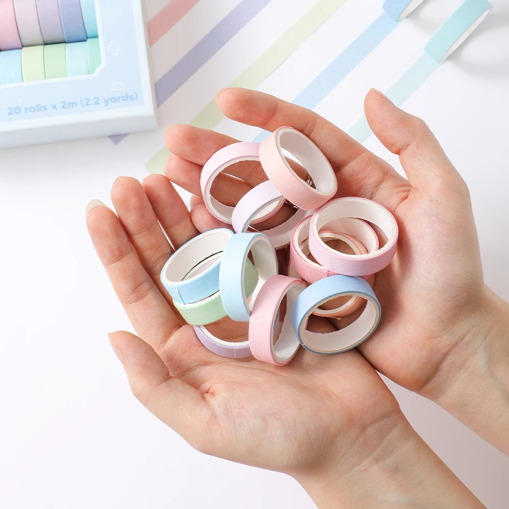 A hand holds a collection of colorful pink, green, and blue washi tape rolls for crafting.