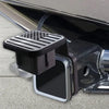 A black trailer hitch receiver cover with a flag emblem is shown attached to a vehicle's hitch.