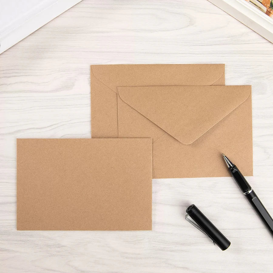Three kraft paper envelopes stacked on a light wooden surface with a black pen.