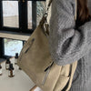 A person wearing a gray sweater holds a beige vintage matte leather crossbody hobo bag.