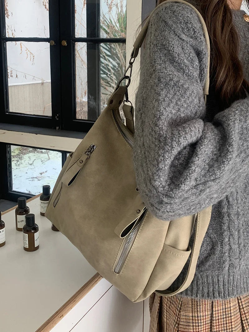 A person wearing a gray sweater holds a beige vintage matte leather crossbody hobo bag.