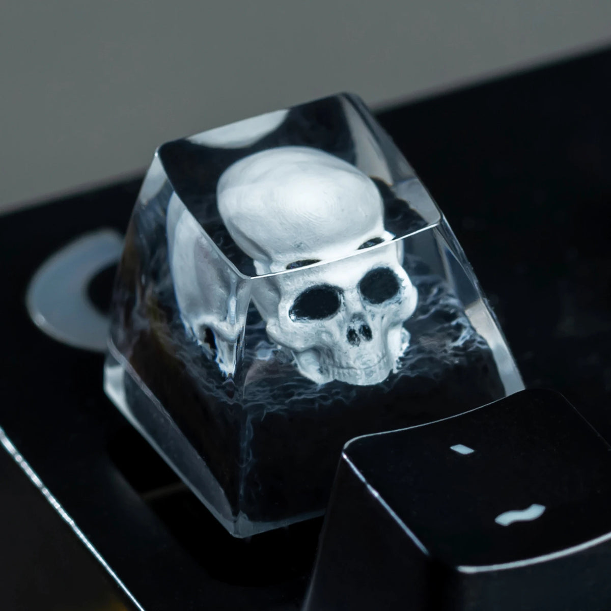 Un capuchon de clavier en résine clair, forme crâne, posé sur une surface de clavier mécanique noire.