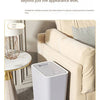 A white pop-up slim trash can is shown next to a sofa in a living room setting.