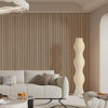 A modern living room featuring a light wood slat wall panel and a tall, sculptural white lamp.