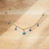 A delicate gold alloy chain with blue feather and star charms hanging against a light wooden background.