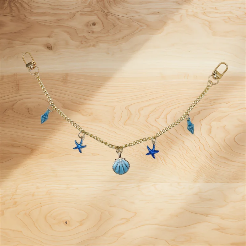 A delicate gold alloy chain with blue feather and star charms hanging against a light wooden background.