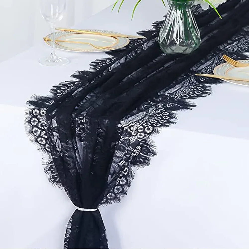 Black embroidered floral lace table runner draped on a white tablecloth with gold plates and a glass vase.