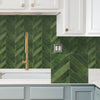 A kitchen backsplash featuring a green diagonal tile pattern under white cabinets and a light countertop.