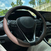 A close-up view of a black steering wheel with a tan leather cover installed in a car interior.