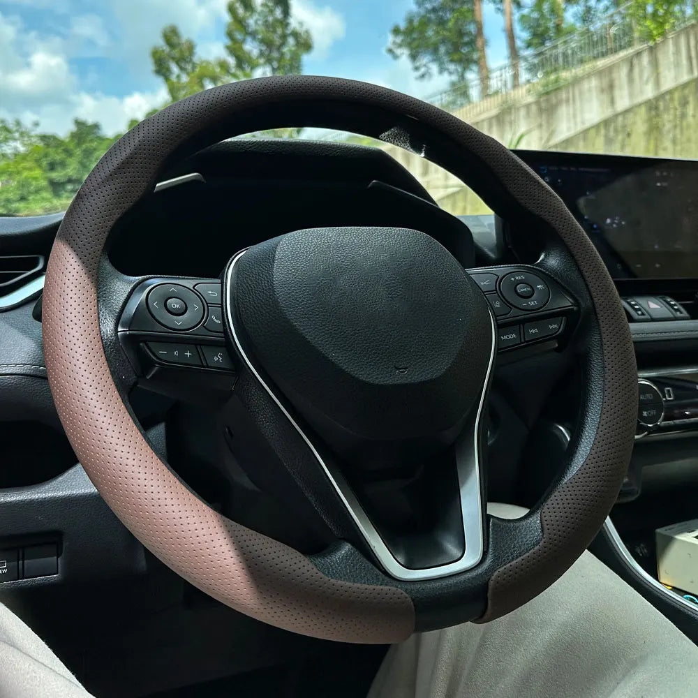 A close-up view of a black steering wheel with a tan leather cover installed in a car interior.