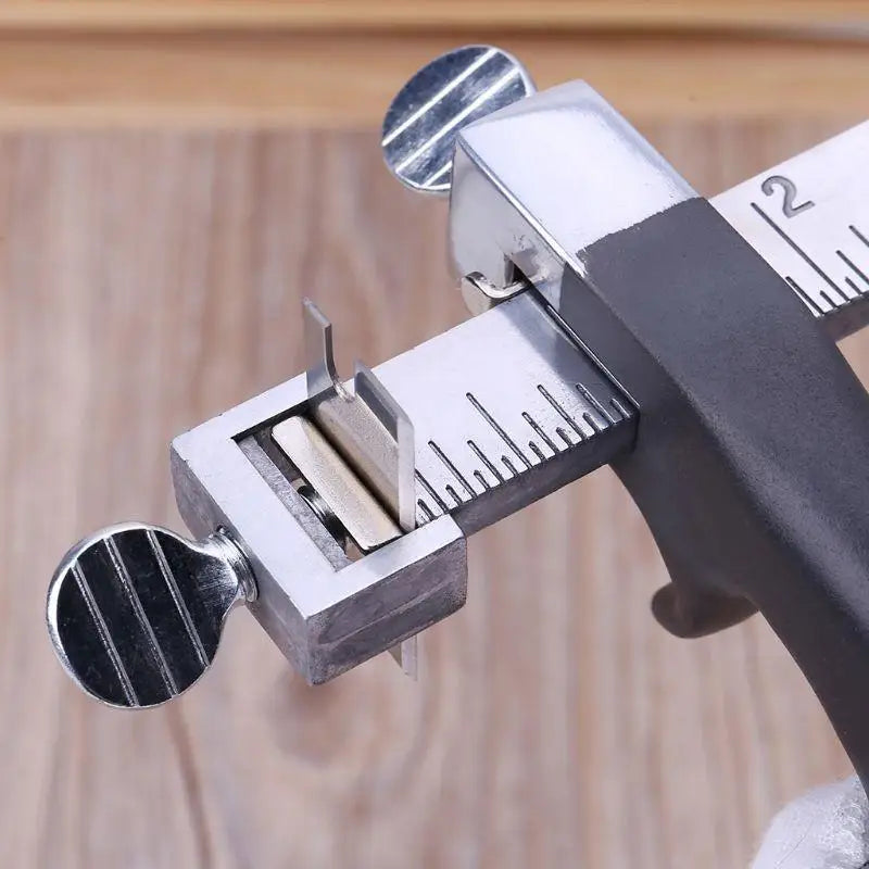 A close-up of an adjustable leather strap cutter with a metal body and two spare blades resting on the cutting mechanism.