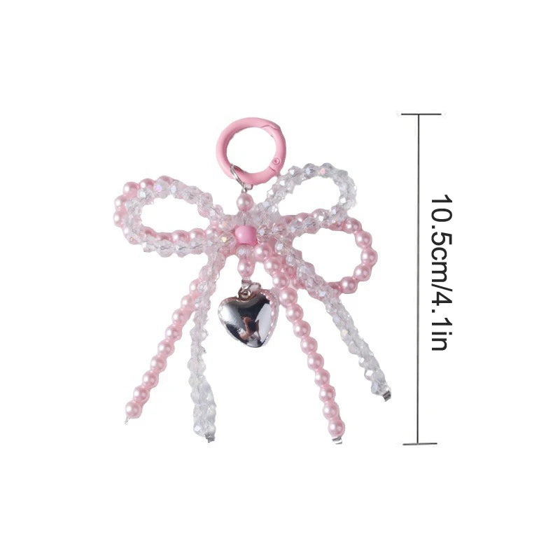 A pink pearl bow keychain featuring a heart charm, displayed against a white background.