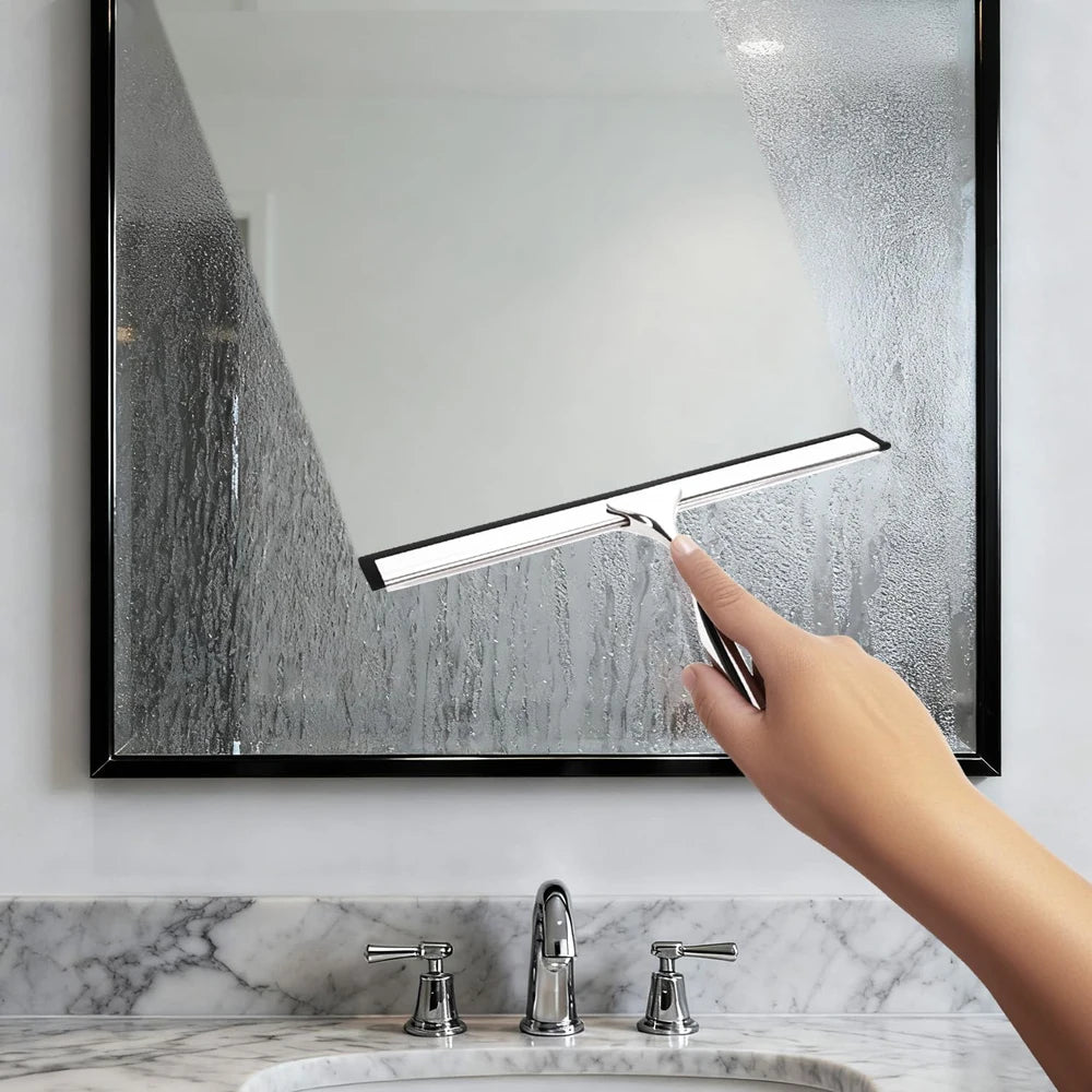 A hand uses a soft silicone shower squeegee with a hanging hook to clean a glass mirror.