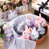 A collection of soft plush bunny toys in various shades of purple, pink, and gray are displayed in a woven basket.