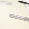 A close-up of an aluminium triangular scale ruler marked with measurements on a lined paper.