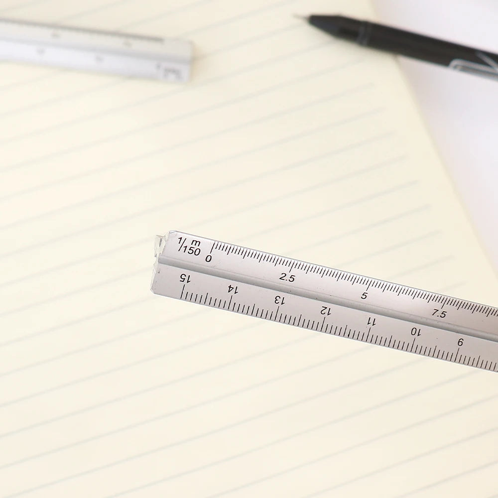 A close-up of an aluminium triangular scale ruler marked with measurements on a lined paper.