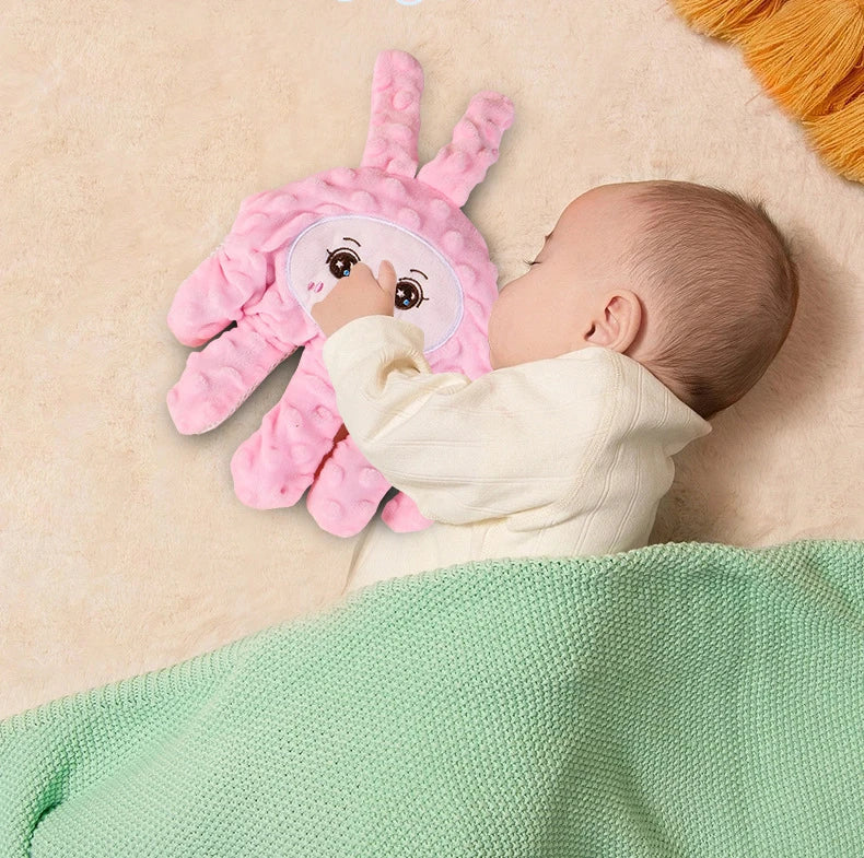 A baby is interacting with a pink palm-shaped sensory toy on a light background.