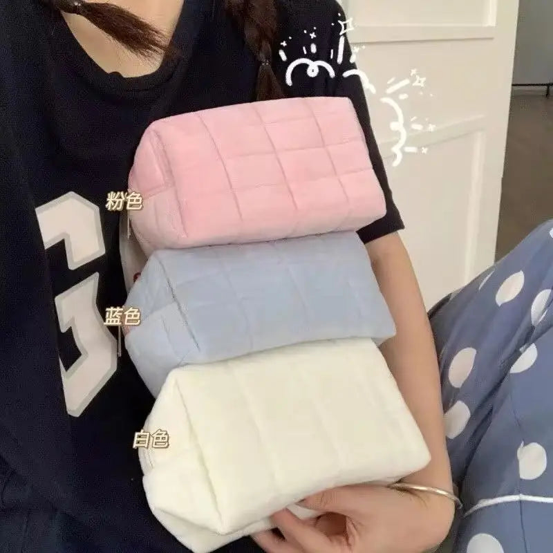 A hand holds a stack of four pink, blue, and white portable makeup bags against a dark shirt.