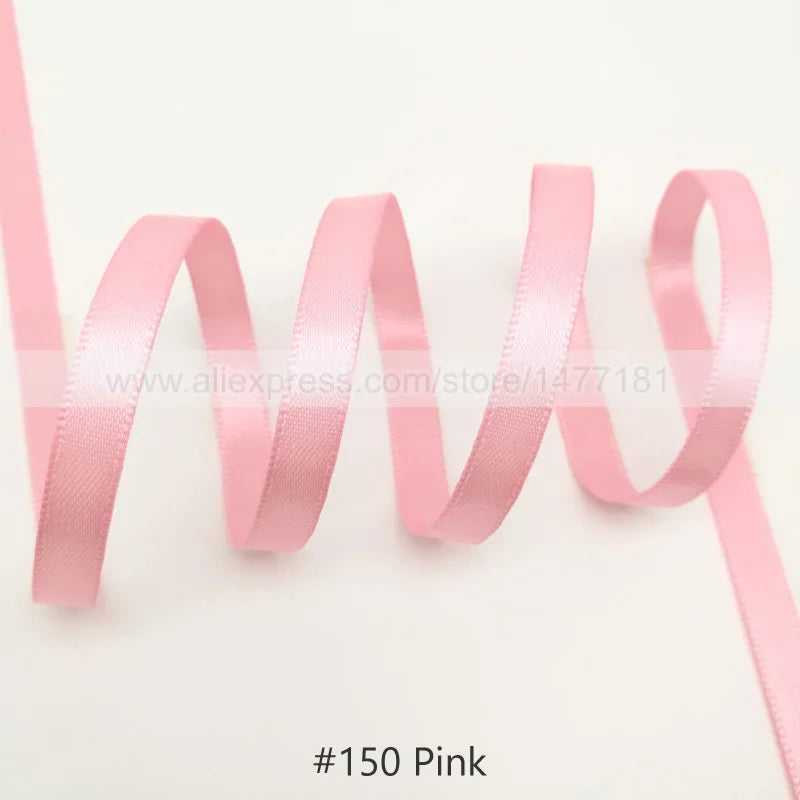 Pink satin ribbon looped and unwound against a white background
