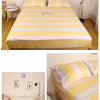 Yellow and striped fitted bed sheet with an elastic band shown on a bed.