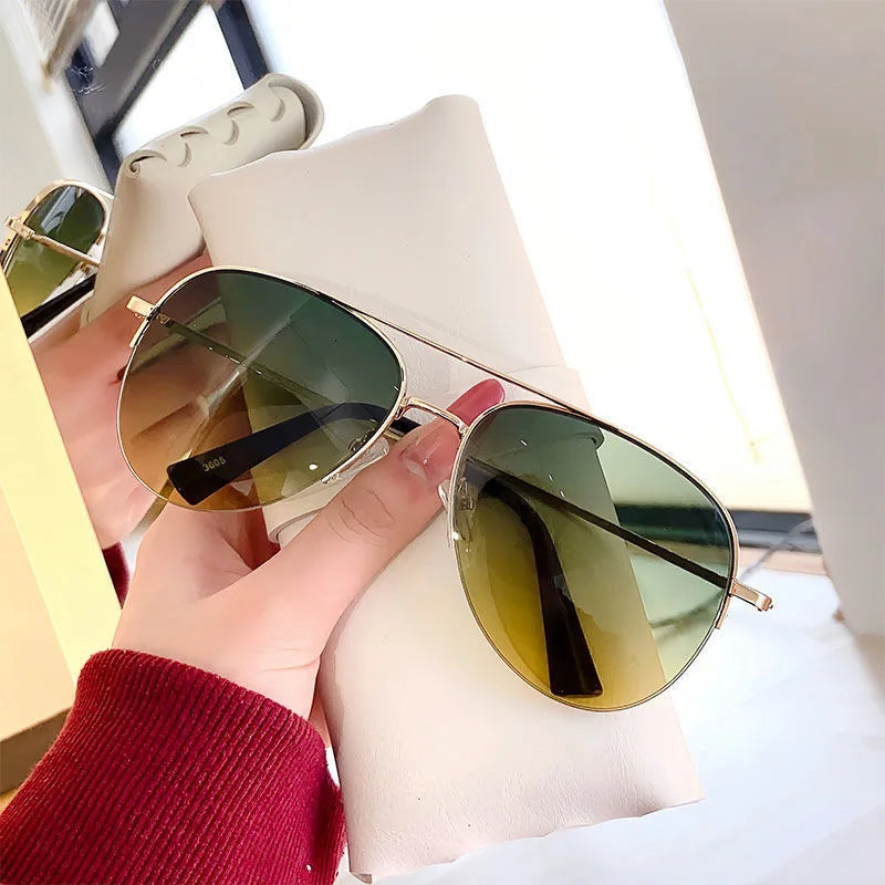 Eine Hand hält eine klassische Aviator-Sonnenbrille mit goldenen Akzenten vor weißem Hintergrund.