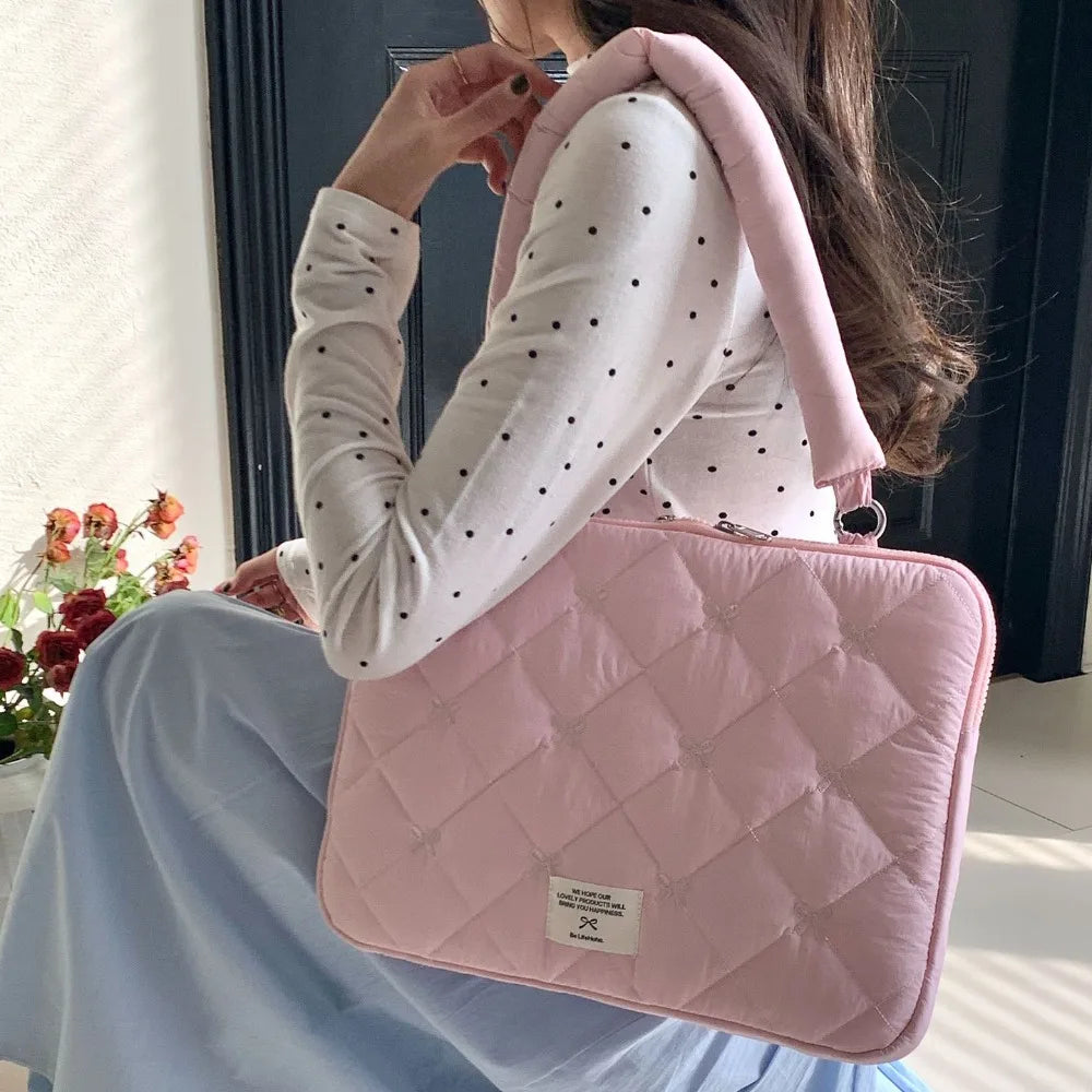 A woman holds a pink quilted laptop shoulder bag with padded protection against her chest.