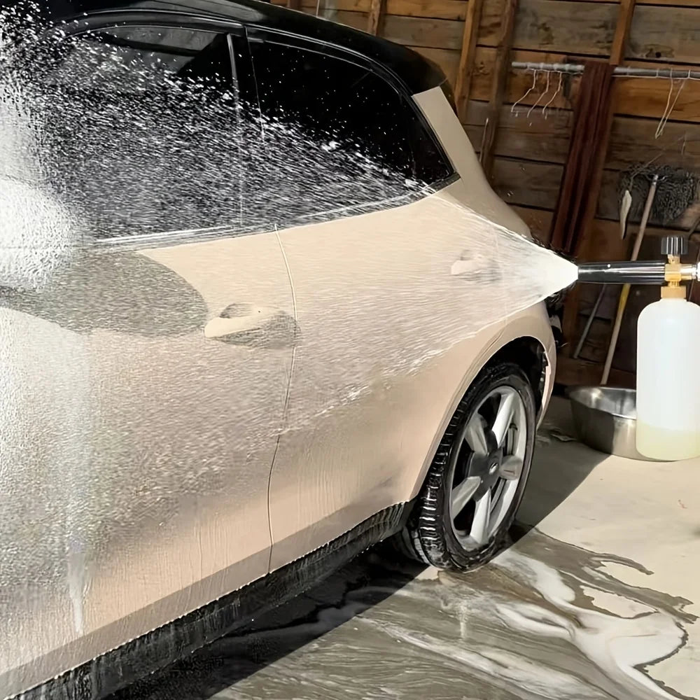 A silver car is being washed by a heavy-duty pressure washer, creating a foam spray on the body.