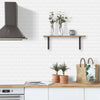A kitchen backsplash featuring white subway tiles, a wooden shelf with potted greenery, and a stainless steel hood.