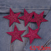 A set of five pink glitter star iron-on embroidered patches placed on a denim fabric.