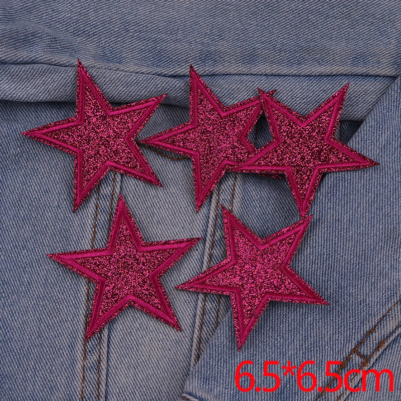 A set of five pink glitter star iron-on embroidered patches placed on a denim fabric.